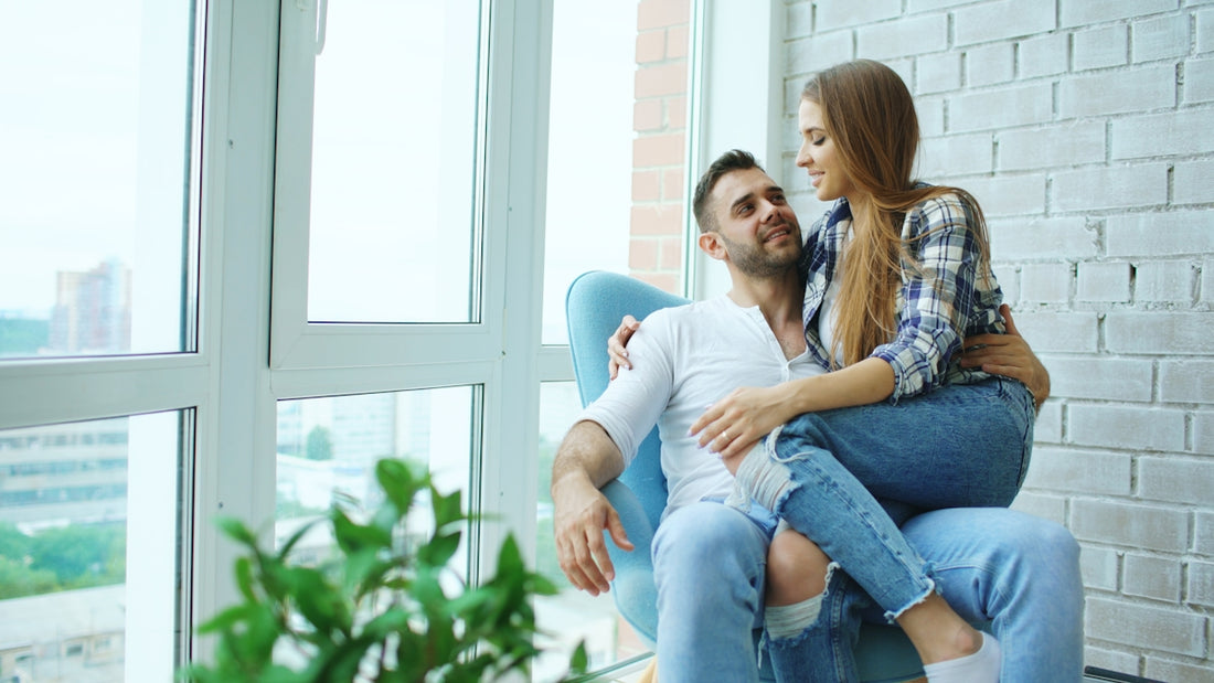 Couple sitting together in a chair by window.