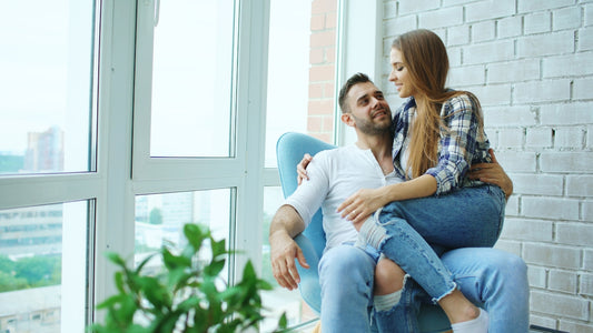 Couple sitting together in a chair by window.